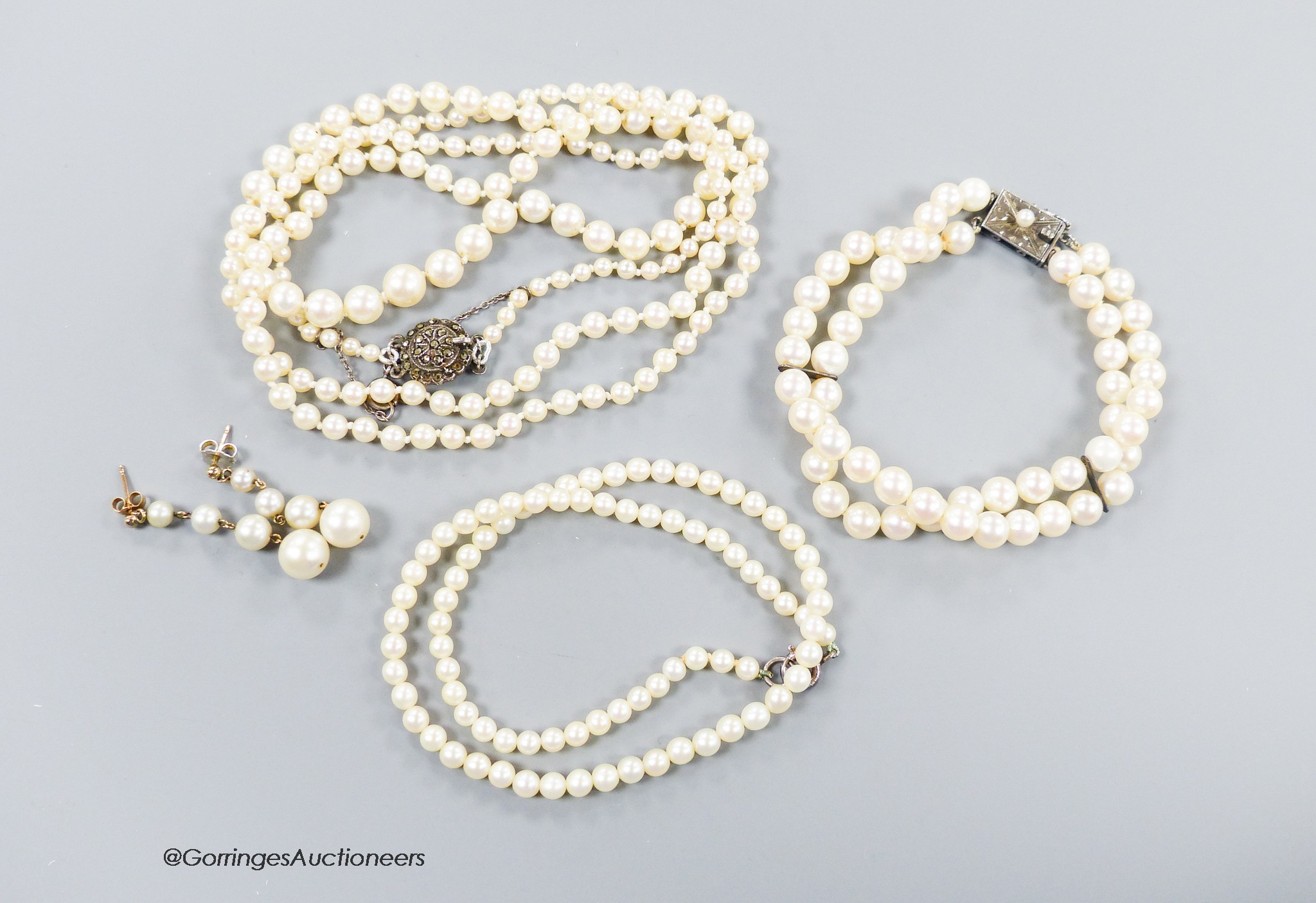 A long single strand graduated cultured pearl necklace, with marcasite clasp, 90cm, one other similar smaller necklace, a similar double strand bracelet and a pair of earrings(a.f.).